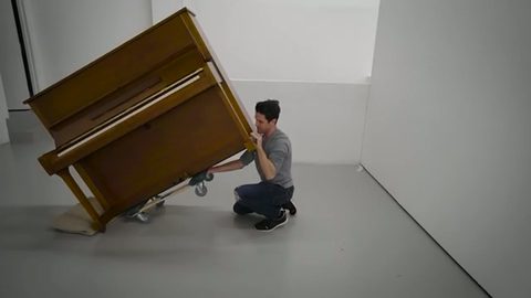 a man rolls an upright piano across a floor on a piano dolly
