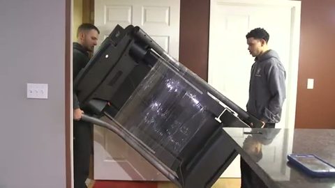 two movers carrying a wrapped treadmill through an interior doorway, face visible