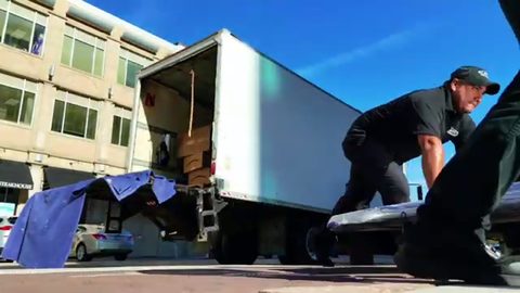 mover unloading a wrapped conference table from a box truck, face visible