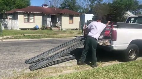 mover positioning loading ramps at the tailgate of a pickup with a mower in the bed